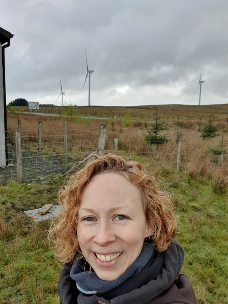 Portrait of Judith Homan with 3 wind turbines in a field in the background
