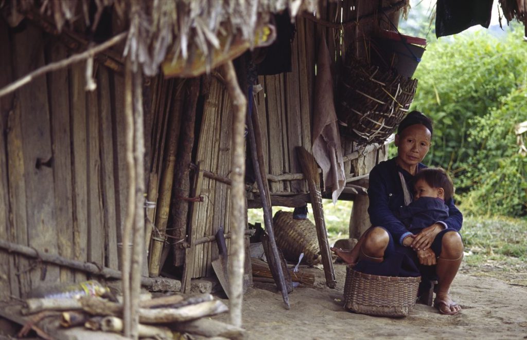 A person sits outside a wooden house.