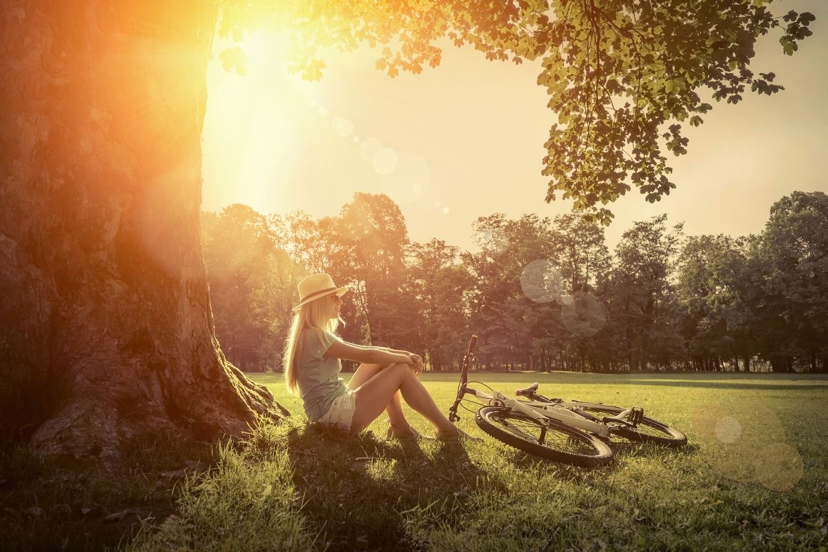 a woman sitting under a tree in bright sunshine