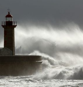 Spray from a wave is blown over a lighthouse on the coast
