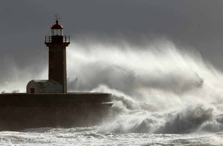 Spray from a wave is blown over a lighthouse on the coast