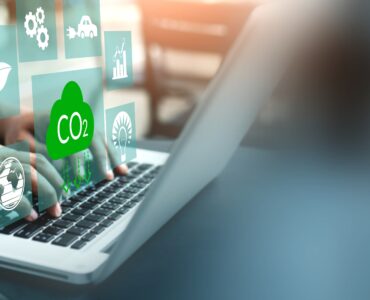 Hands type on the keyboard of a laptop with symbols overlaid representing CO2, energy, emissions, climate.