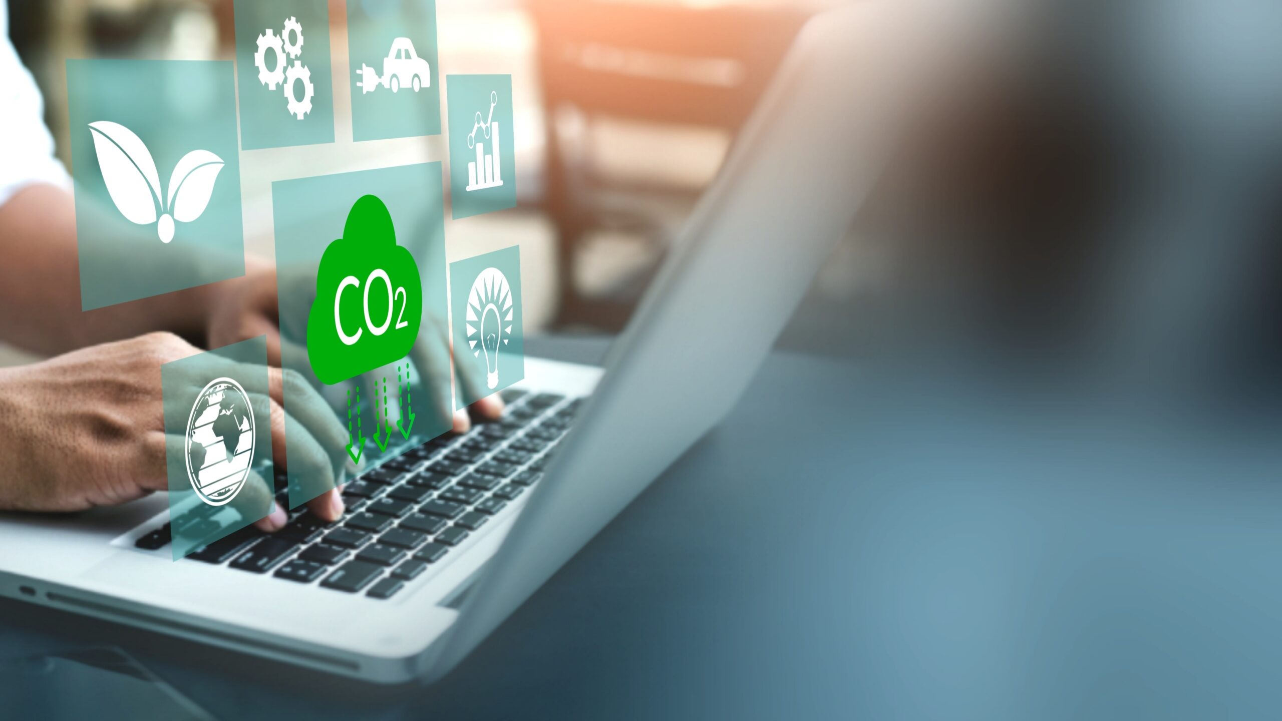 Hands type on the keyboard of a laptop with symbols overlaid representing CO2, energy, emissions, climate.