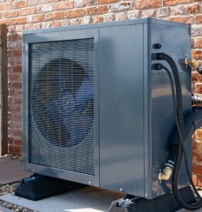 A heat pump against the outside wall of a brick building.