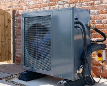 A heat pump against the outside wall of a brick building.