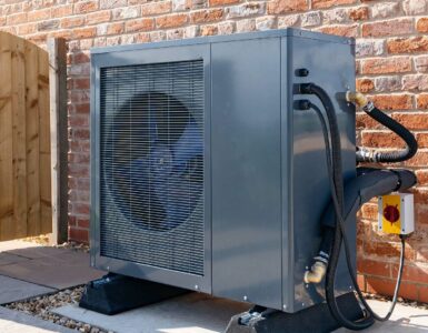 A heat pump against the outside wall of a brick building.