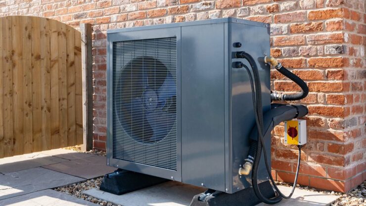 A heat pump against the outside wall of a brick building.